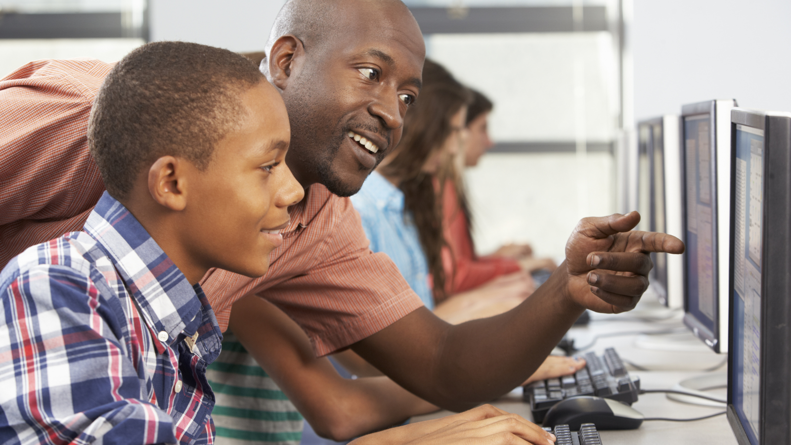 High school student working on computer at school with the help of teacher