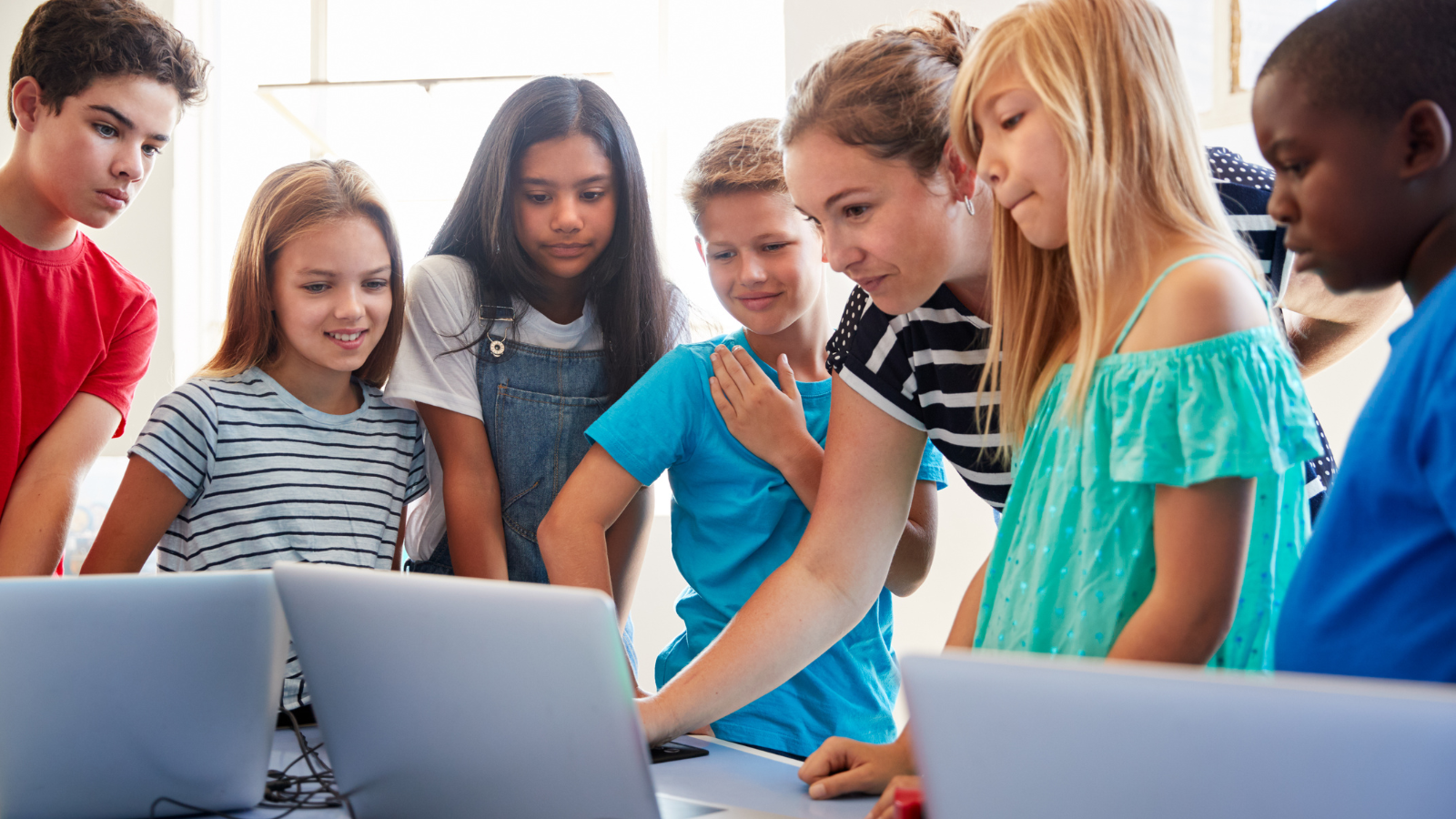 Elementary school students working on computers with help of teacher